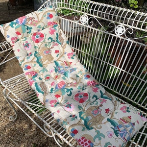 May include: A white bench cushion with a floral pattern featuring elephants, flowers, and geometric designs in shades of pink, green, and gold.