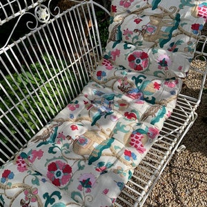 May include: White metal garden bench with a floral patterned cushion. The cushion has a white background with pink, red, and green floral designs.