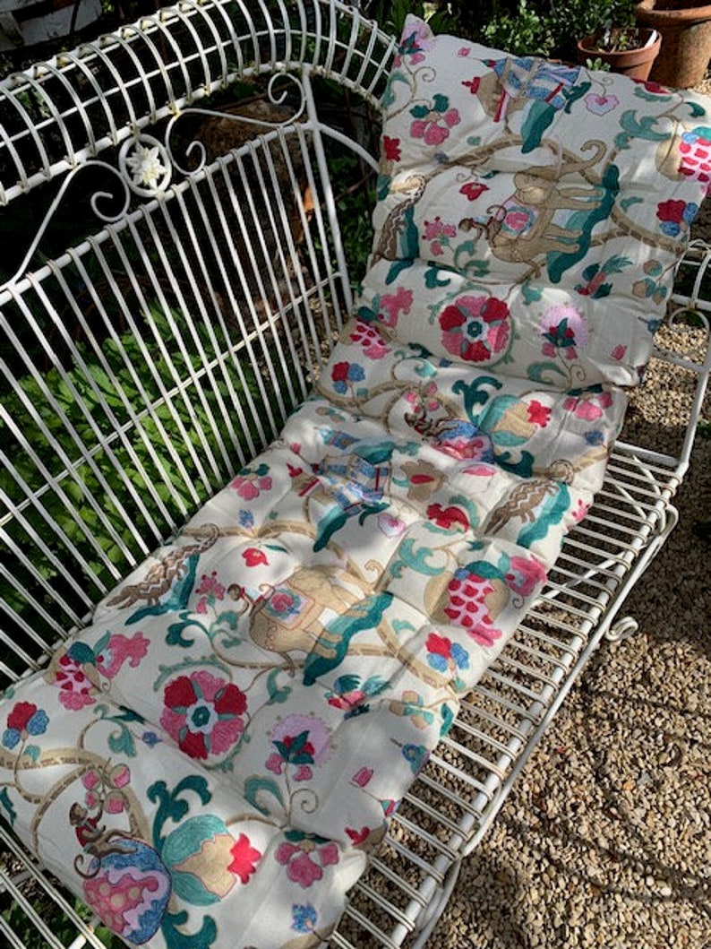 May include: White metal garden bench with a floral patterned cushion. The cushion has a white background with pink, red, and green floral designs.