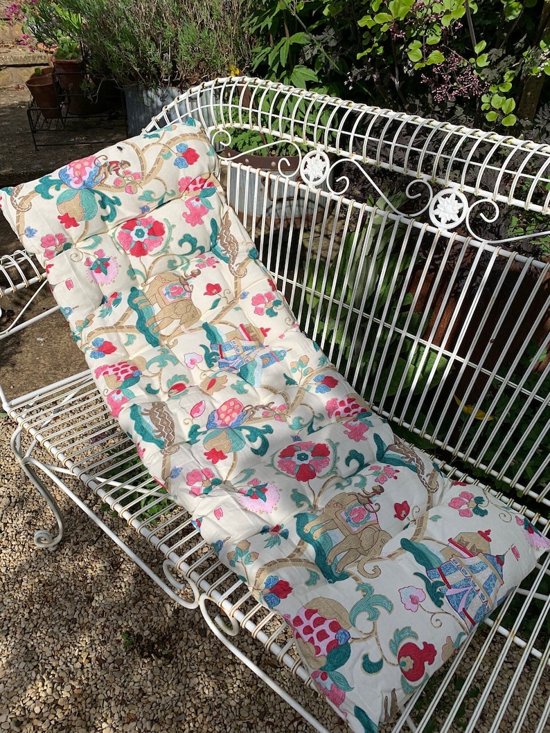 May include: A white bench cushion with a floral pattern featuring elephants, flowers, and geometric designs in shades of pink, green, and gold.