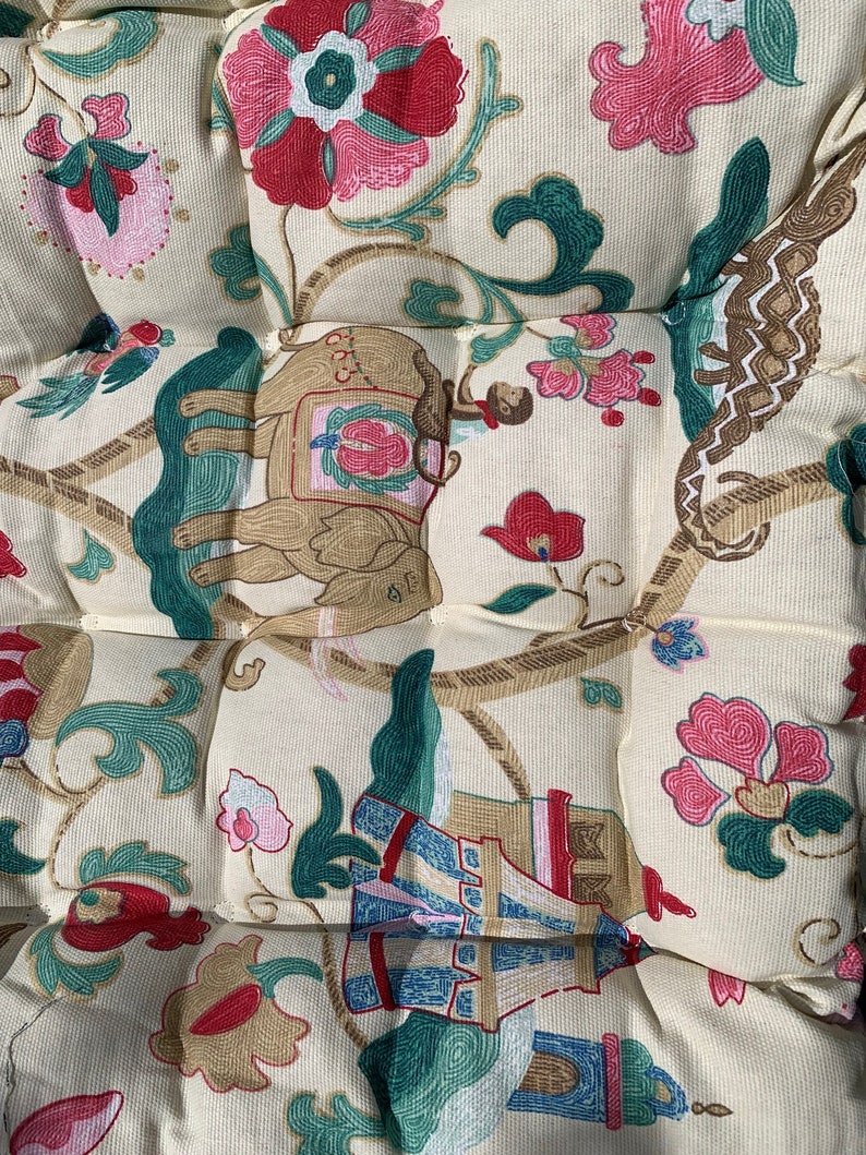 May include: A cream-coloured fabric with a repeating pattern of green, brown, and pink floral designs. The pattern also includes an elephant, a monkey, and a tower.