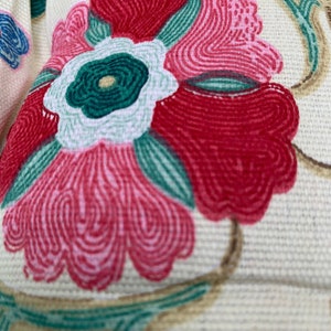May include: Close-up of a floral pattern on a cream-coloured fabric. The flower is pink, red, and green with a white centre.