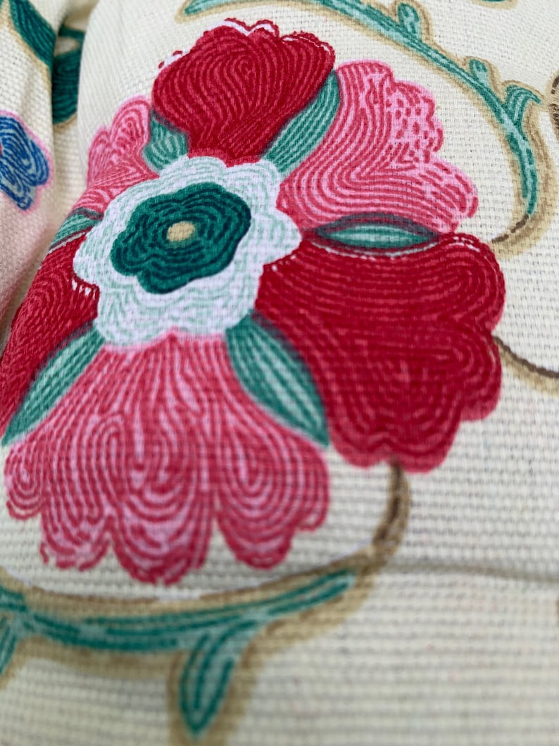 May include: Close-up of a floral pattern on a cream-coloured fabric. The flower is pink, red, and green with a white centre.
