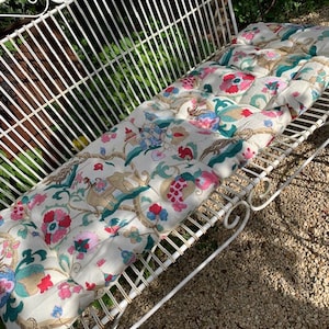 May include: A white metal garden bench with a floral patterned cushion. The cushion has pink, green, blue, and gold accents.