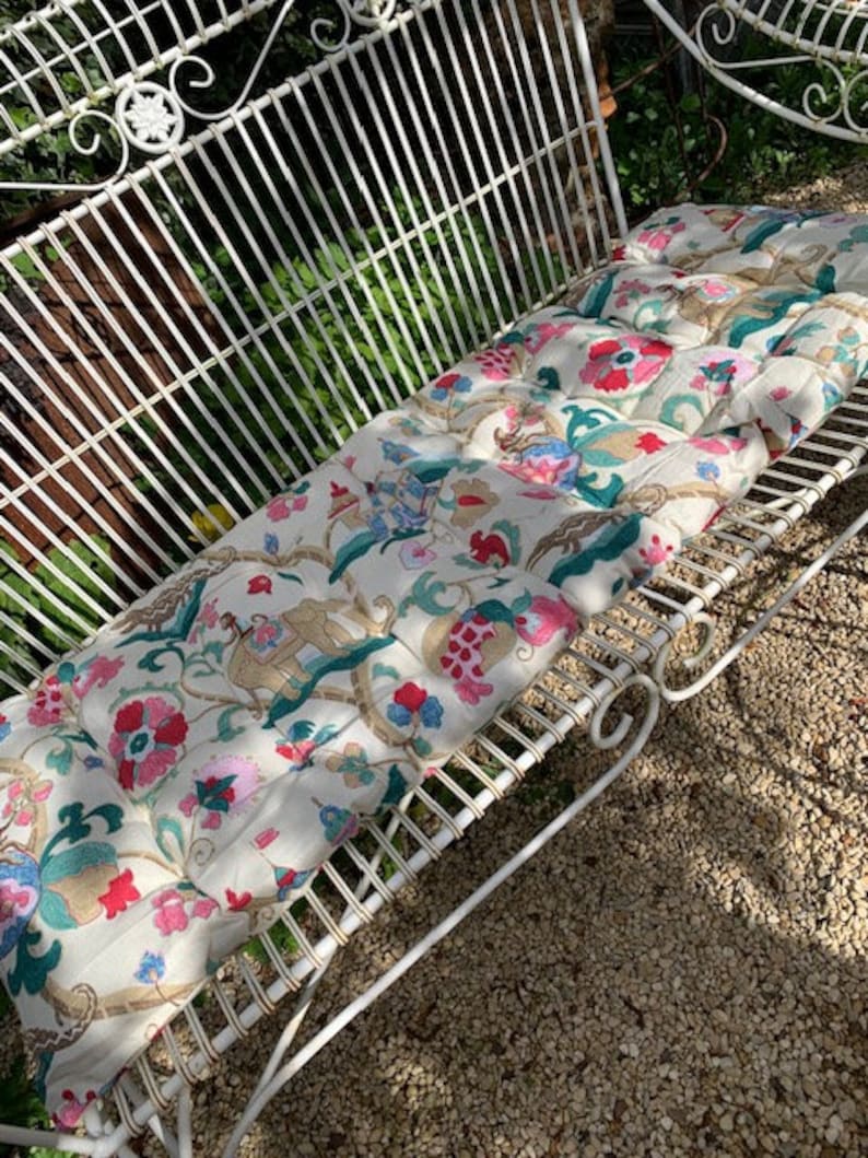 May include: A white metal garden bench with a floral patterned cushion. The cushion has pink, green, blue, and gold accents.
