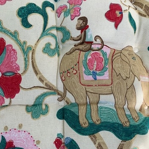 May include: A cream-coloured fabric with a repeating pattern of pink and red flowers, green leaves, and a brown elephant with a monkey riding on its back.