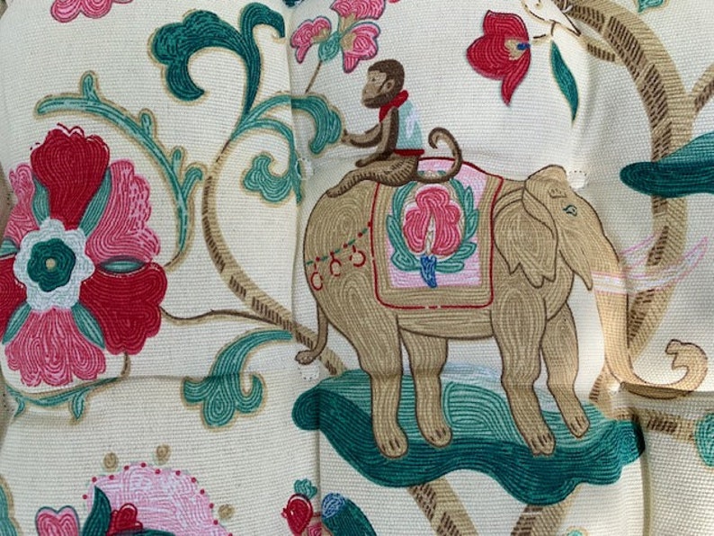May include: A cream-coloured fabric with a repeating pattern of pink and red flowers, green leaves, and a brown elephant with a monkey riding on its back.