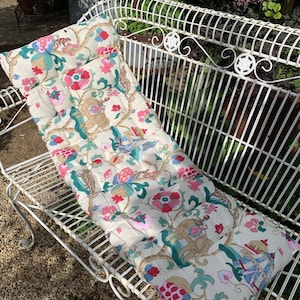 May include: A white metal bench with a floral patterned cushion. The cushion has pink, green, and blue flowers and a gold design.