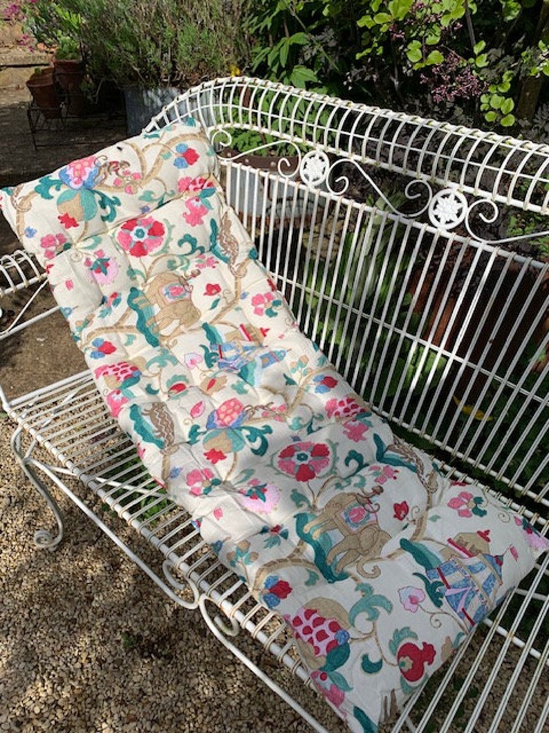 May include: A white metal bench with a floral patterned cushion. The cushion has pink, green, and blue flowers and a gold design.