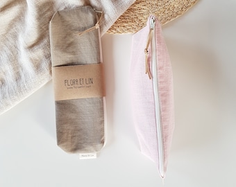 Op de afbeelding: Twee linnen pouches, één in lichtroze en de andere in neutraal beige, worden gepresenteerd tegen een neutrale achtergrond. De roze pouch heeft een witte rits en een leren trekker. De beige pouch is verpakt met een bruine papieren band met de tekst "FLORA ET LIN".