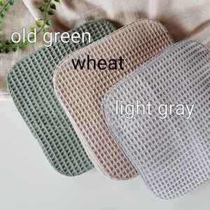 Pu&ograve; includere: Tre strofinacci in tessuto a nido d'ape di diversi colori: verde scuro, grano e grigio chiaro. Gli strofinacci sono piegati e disposti in fila.