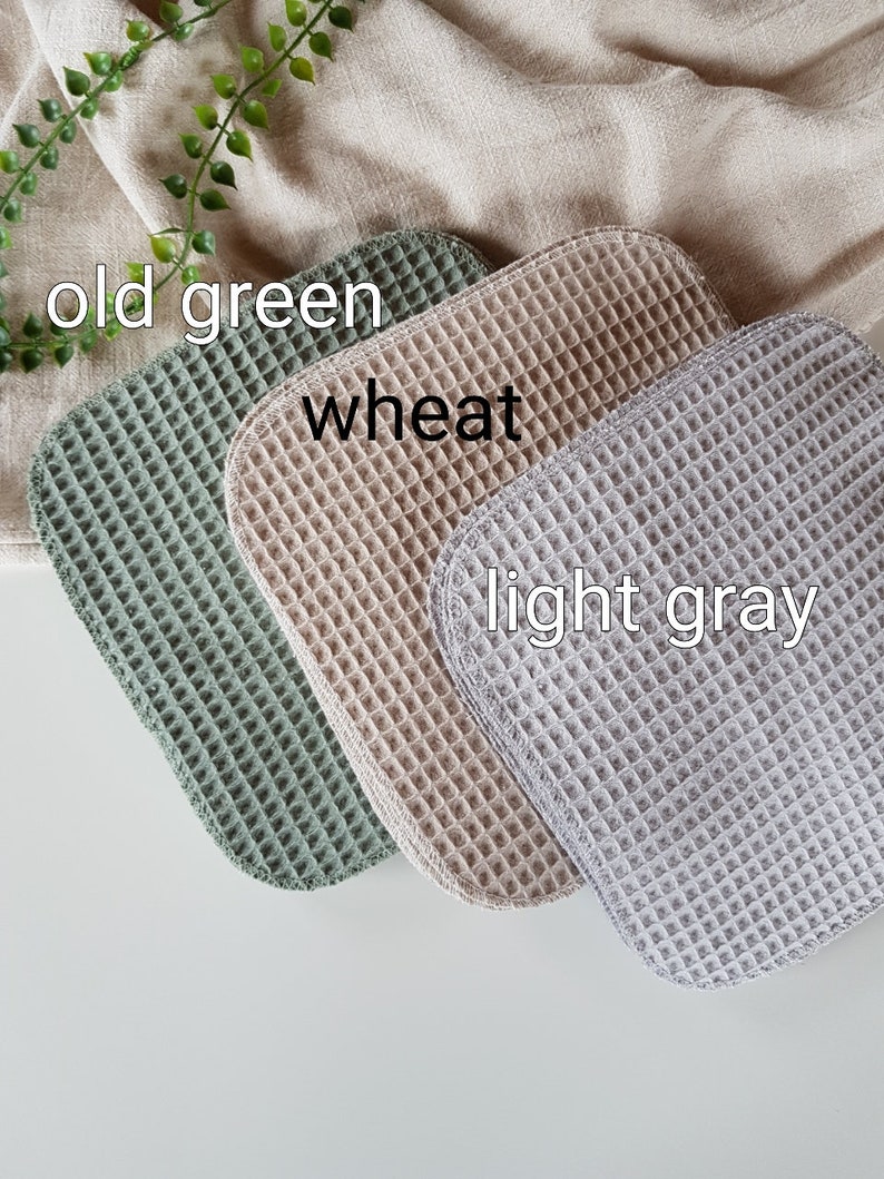Pu&ograve; includere: Tre strofinacci in tessuto a nido d'ape di diversi colori: verde scuro, grano e grigio chiaro. Gli strofinacci sono piegati e disposti in fila.