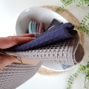 May include: Two waffle weave kitchen towels, one gray and one dark blue, folded and stacked on top of each other. The towels are made of a soft, absorbent material and are perfect for drying dishes, hands, and surfaces.