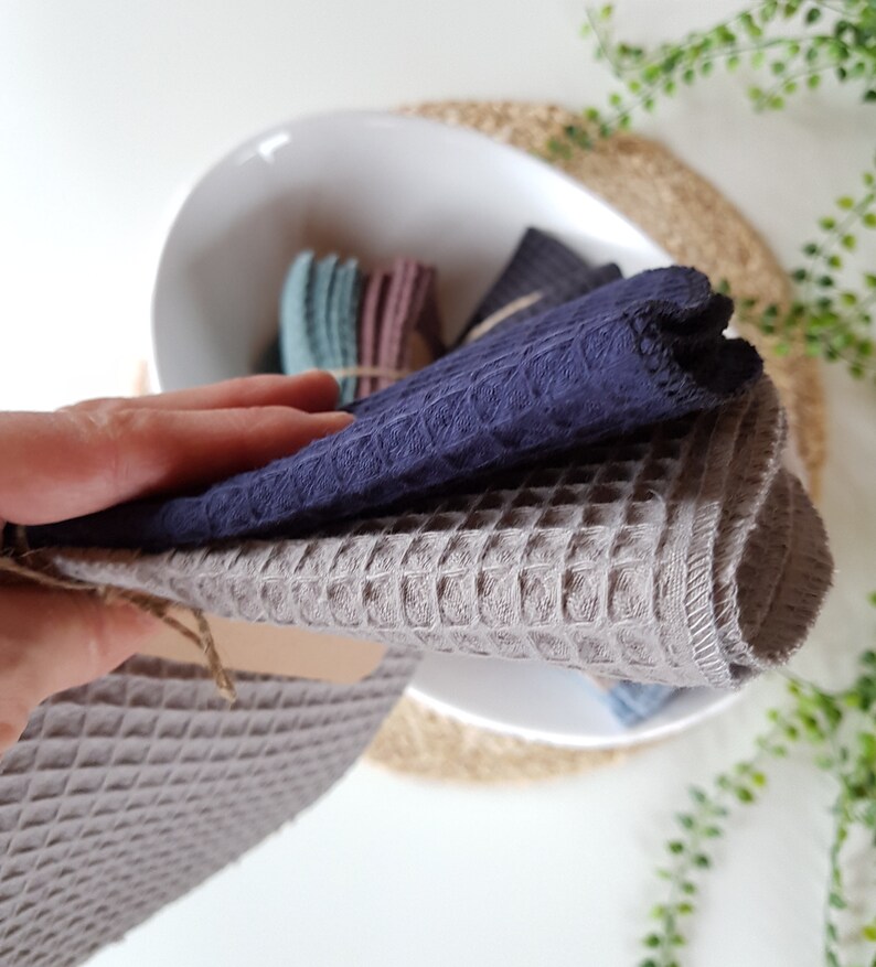 May include: Two waffle weave kitchen towels, one gray and one dark blue, folded and stacked on top of each other. The towels are made of a soft, absorbent material and are perfect for drying dishes, hands, and surfaces.