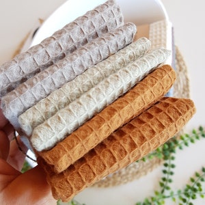 May include: A stack of four waffle weave fabric squares in beige, light green, and brown.