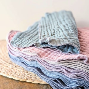 May include: A stack of soft, textured cloths in shades of blue and pink. The cloths are folded and arranged in a pyramid shape.