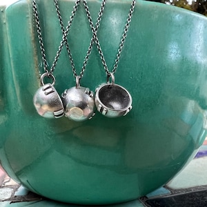 May include: Three silver necklaces with round pendants hanging from a green ceramic bowl. The pendants are all different shapes and sizes.