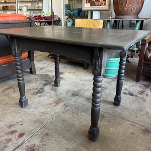 May include: A dark brown wooden table with a rectangular top and four turned legs. The table is made of solid wood and has a simple, classic design. The legs are intricately carved with a spiral pattern. The table is likely an antique or vintage piece.