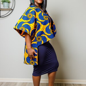 May include: A woman wearing a yellow and blue patterned kimono-style top over a navy blue skirt and black heeled sandals with gold chains.