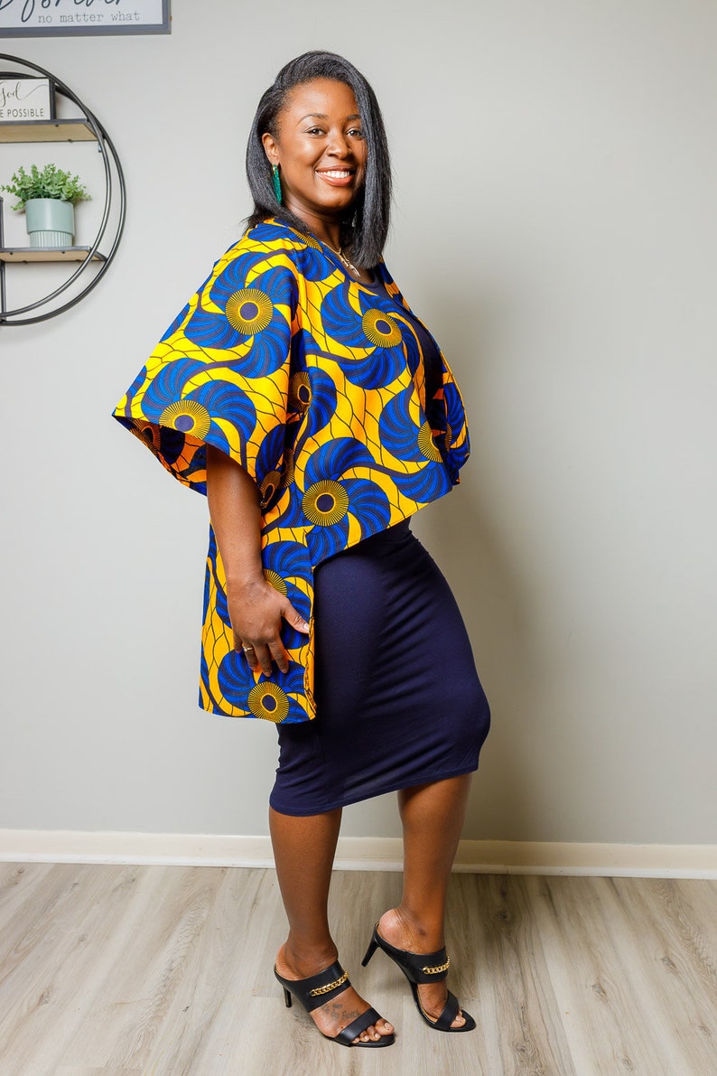 May include: A woman wearing a yellow and blue patterned kimono-style top over a navy blue skirt and black heeled sandals with gold chains.