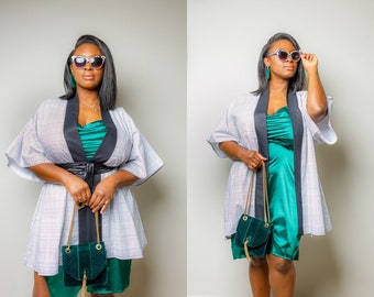 May include: A woman wearing a white and black patterned kimono with a green satin dress underneath. She is holding a green velvet handbag with a gold chain strap.