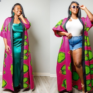 May include: A vibrant, long kimono in a magenta and green pattern. The kimono features a black trim and is worn over a teal dress and denim shorts. The design includes a repeating pattern of green shapes on a magenta background.