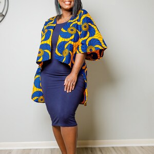 May include: A woman wearing a blue and yellow patterned kimono-style jacket over a navy blue dress. She is wearing black heeled sandals with gold chain accents.