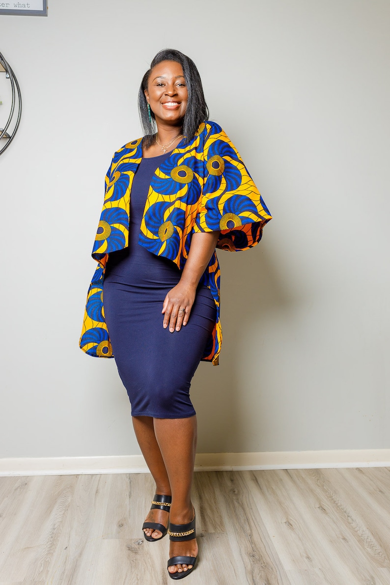 May include: A woman wearing a blue and yellow patterned kimono-style jacket over a navy blue dress. She is wearing black heeled sandals with gold chain accents.