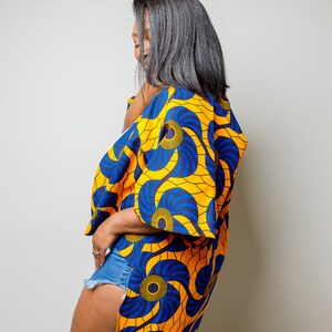 May include: A woman wearing a blue and yellow patterned kimono with a side slit. The kimono has a floral design with blue and yellow swirls.