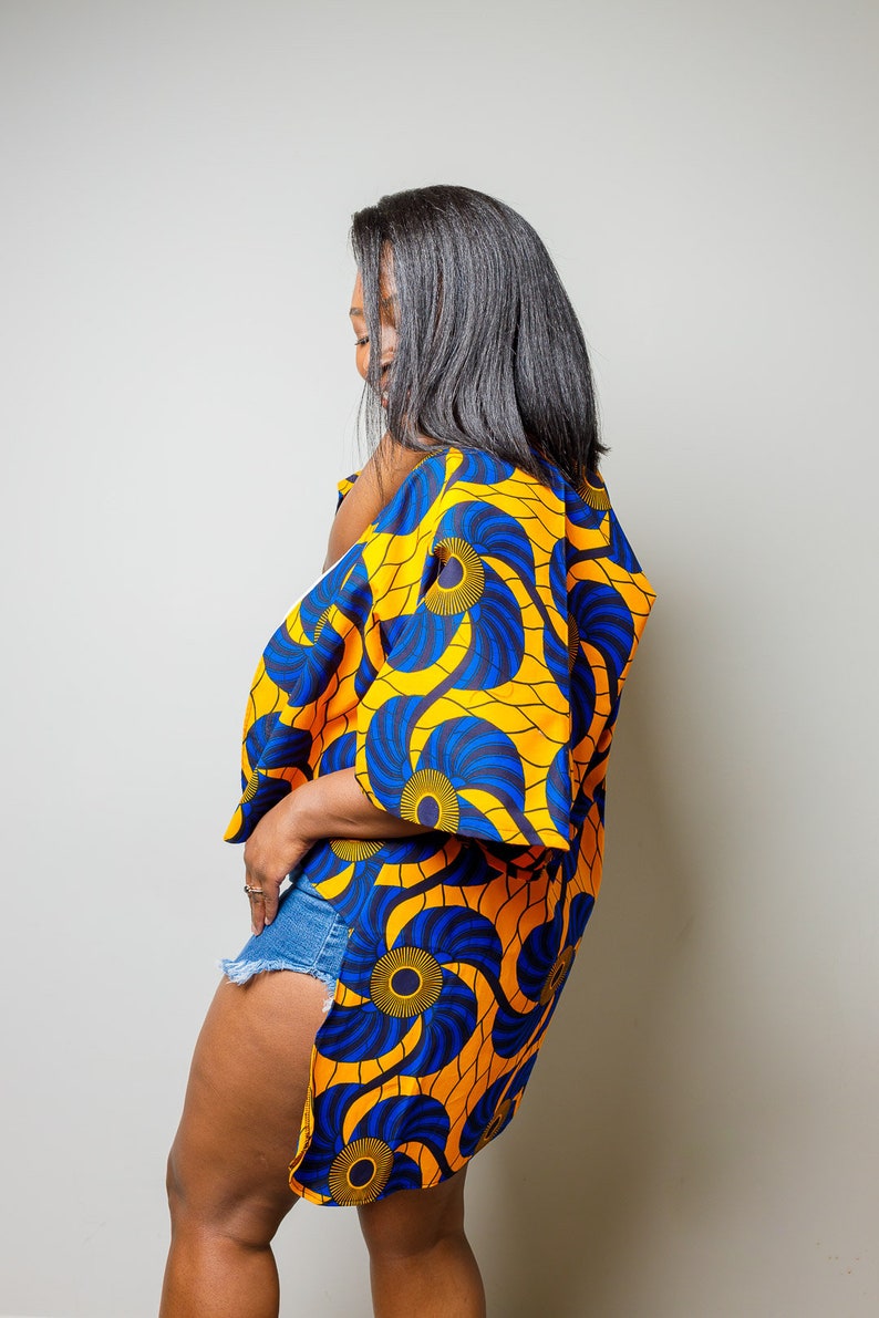 May include: A woman wearing a blue and yellow patterned kimono with a side slit. The kimono has a floral design with blue and yellow swirls.