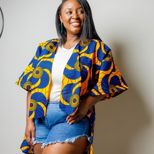 May include: A woman wearing a yellow and blue patterned kimono with a white t-shirt and denim shorts.