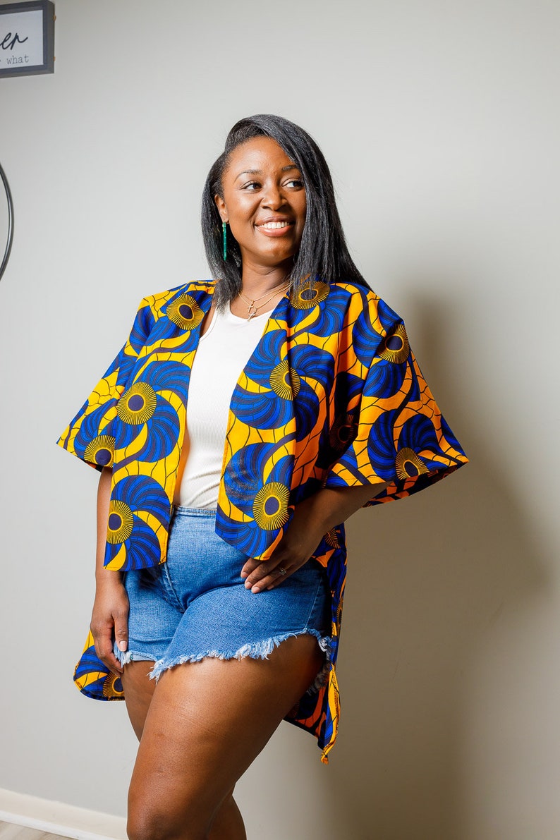 May include: A woman wearing a yellow and blue patterned kimono with a white t-shirt and denim shorts.