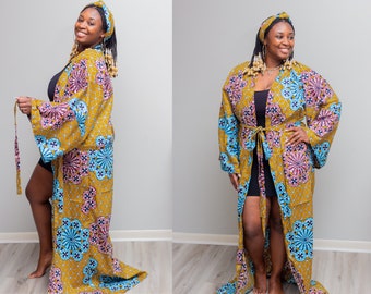 May include: A long, flowing robe and matching head wrap in a vibrant mustard yellow fabric. The robe features a geometric pattern with pink and blue floral designs. The robe has wide sleeves and a matching belt.