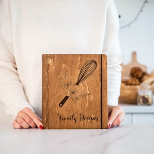 May include: A wooden recipe book with a floral design and a whisk engraved on the cover. The book is labeled "Family Recipes".