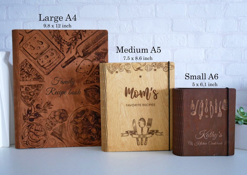 May include: Three wooden recipe books in different sizes. The largest book is brown with a design of food and kitchen items. The middle book is light brown with the text "Mom's Favorite Recipes". The smallest book is dark brown with the text "Kathy's Kitchen Cookbook".