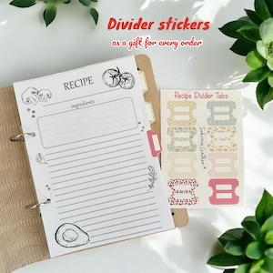 May include: A white recipe binder with a blank recipe page open. The page has a drawing of a tomato, mushroom, and avocado. The binder has a red tab divider. A sheet of recipe divider tabs with floral and gingham patterns is on the right side of the image. The text on the sheet reads "Recipe Divider Tabs" and "Sekvoia Leather".