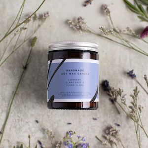 May include: A brown glass jar candle with a silver lid. The label reads "Handmade Soy Wax Candle Lavender, Clary Sage & Ylang Ylang" and "Made from pure essential oils with eco-wick in Co. Down, Ireland www.simplehomeholism.com".