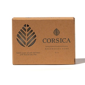 May include: A brown cardboard box with a leaf design cut out. The box contains a 6 oz bar of "Backwoods Soap" by Corsica. The text on the box reads "Subtle scent of oak and moss with French sea clay."