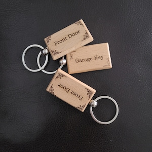 May include: Three wooden keychains with decorative borders and engraved text. The keychains read "Front Door", "Garage Key", and "Front Door".