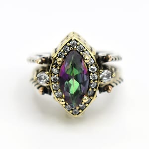 May include: A gold and silver ring with a large, iridescent marquise-shaped gemstone surrounded by smaller clear gemstones.