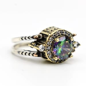 Könnte beinhalten: Ein Silber- und Goldring mit einem großen, schillernden Edelstein, der von kleineren, klaren Edelsteinen umgeben ist. Der Ring hat ein detailliertes Design mit aufwendigen Schnitzereien.
