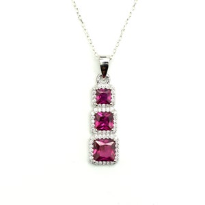 May include: A silver necklace with a pendant featuring three square-shaped pink gemstones surrounded by smaller clear gemstones.