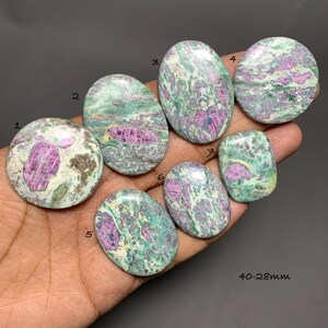 May include: Seven polished cabochons of green zoisite with magenta ruby inclusions, numbered one through seven. The stones feature varied oval and circular shapes with smooth, reflective surfaces. Text on the image indicates 40-28mm.