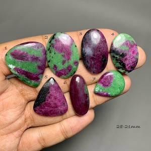 May include: Seven polished ruby zoisite cabochons in various shapes and sizes, ranging from 28-21mm. Each stone displays a unique combination of vibrant magenta-pink ruby inclusions set against a mottled green zoisite matrix with black accents.