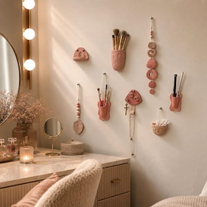 May include: A collection of terracotta-colored wall-mounted organizers and decorative hangings. The set includes face-shaped cups for brushes, a mushroom-shaped hook, a leaf-shaped ornament, and a vertical beaded mobile, all arranged on a neutral wall.