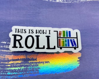 May include: White sticker with the text "This is how I roll" in black. A black and white illustration of a book cart with rainbow colored books is to the right of the text.