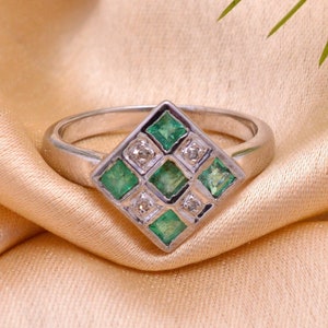 May include: A silver ring with a square-shaped setting featuring a cluster of green emeralds and white diamonds.