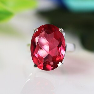 Peut inclure: Une bague en argent ornée d'une grande pierre précieuse rubis ovale et facettée. Le rubis est d'un rouge profond et vibrant, et la bague a un design simple et élégant. La pierre mesure environ 2,5 cm de long.
