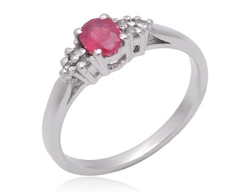 May include: A silver ring with a red oval gemstone and smaller clear gemstones set around it.
