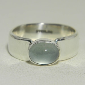 May include: A silver ring with a light blue gemstone set in a bezel setting. The ring has a wide band.